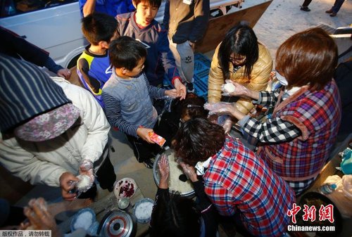 當地時間4月17日，志愿者在公園的空地上制作飯團發放給小朋友。