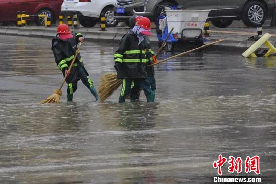 圖為環(huán)衛(wèi)工人們冒雨清掃路面。　鄧建青 攝